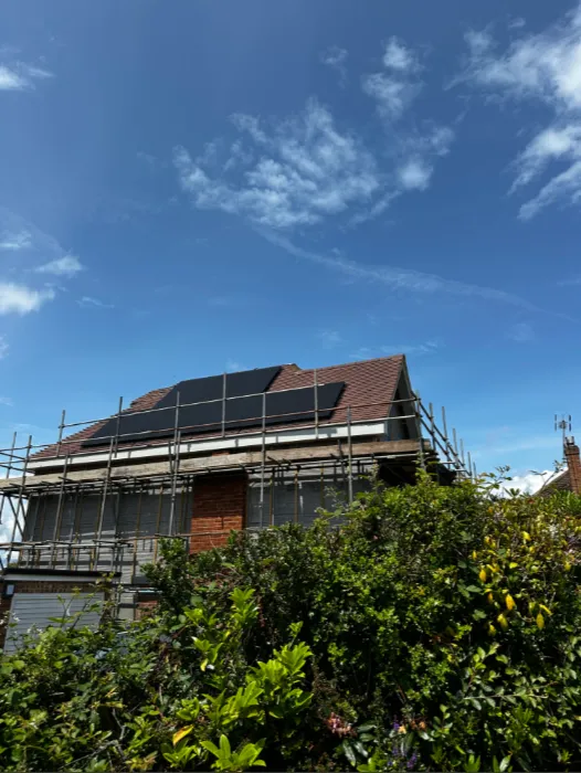Newly installed solar panels on a roof of a house in the sunlight with a dark blue sky in the background. There is scaffolding around the house